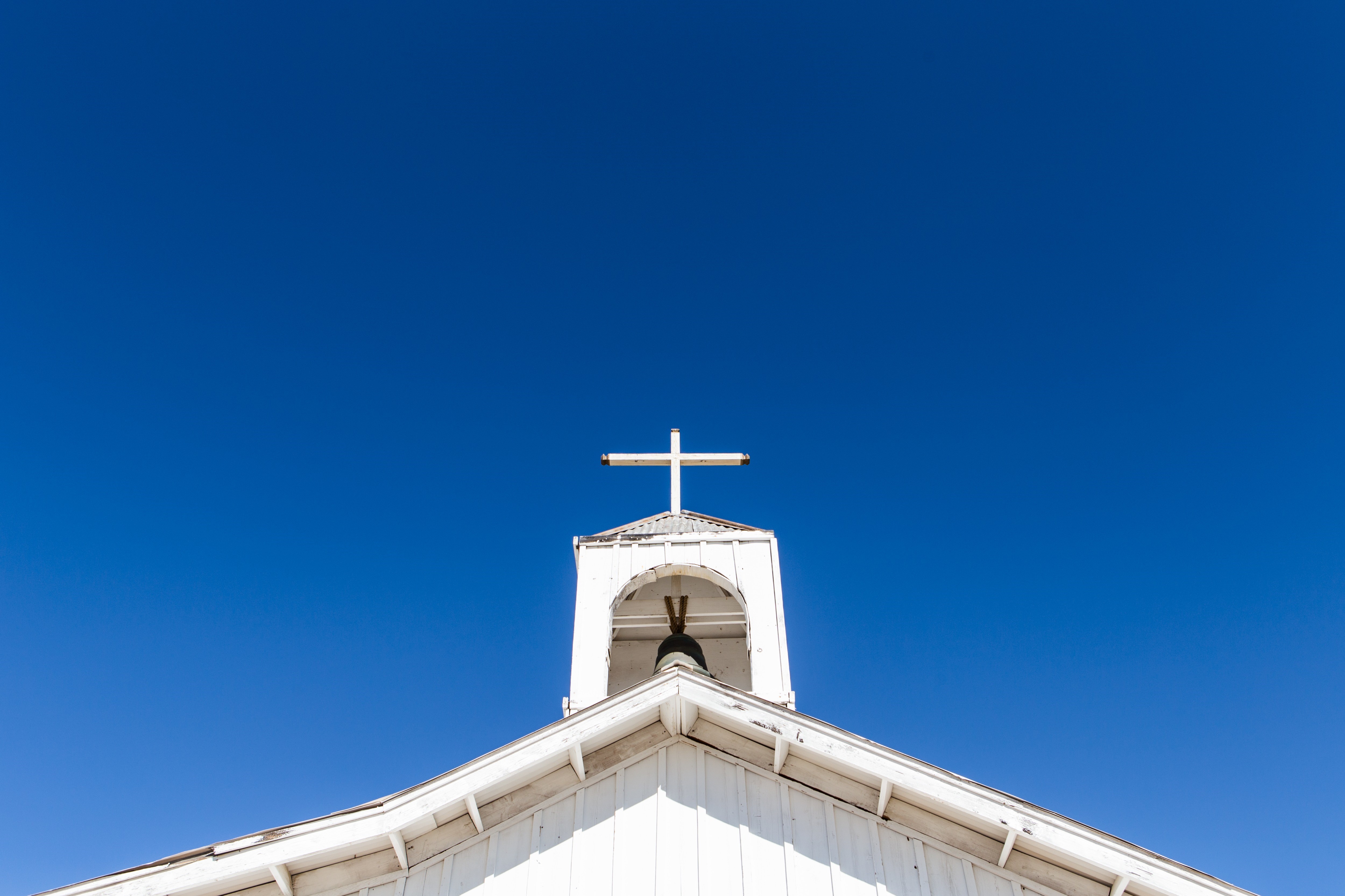 Photo of a church steeple with church bell and cross on the top. 