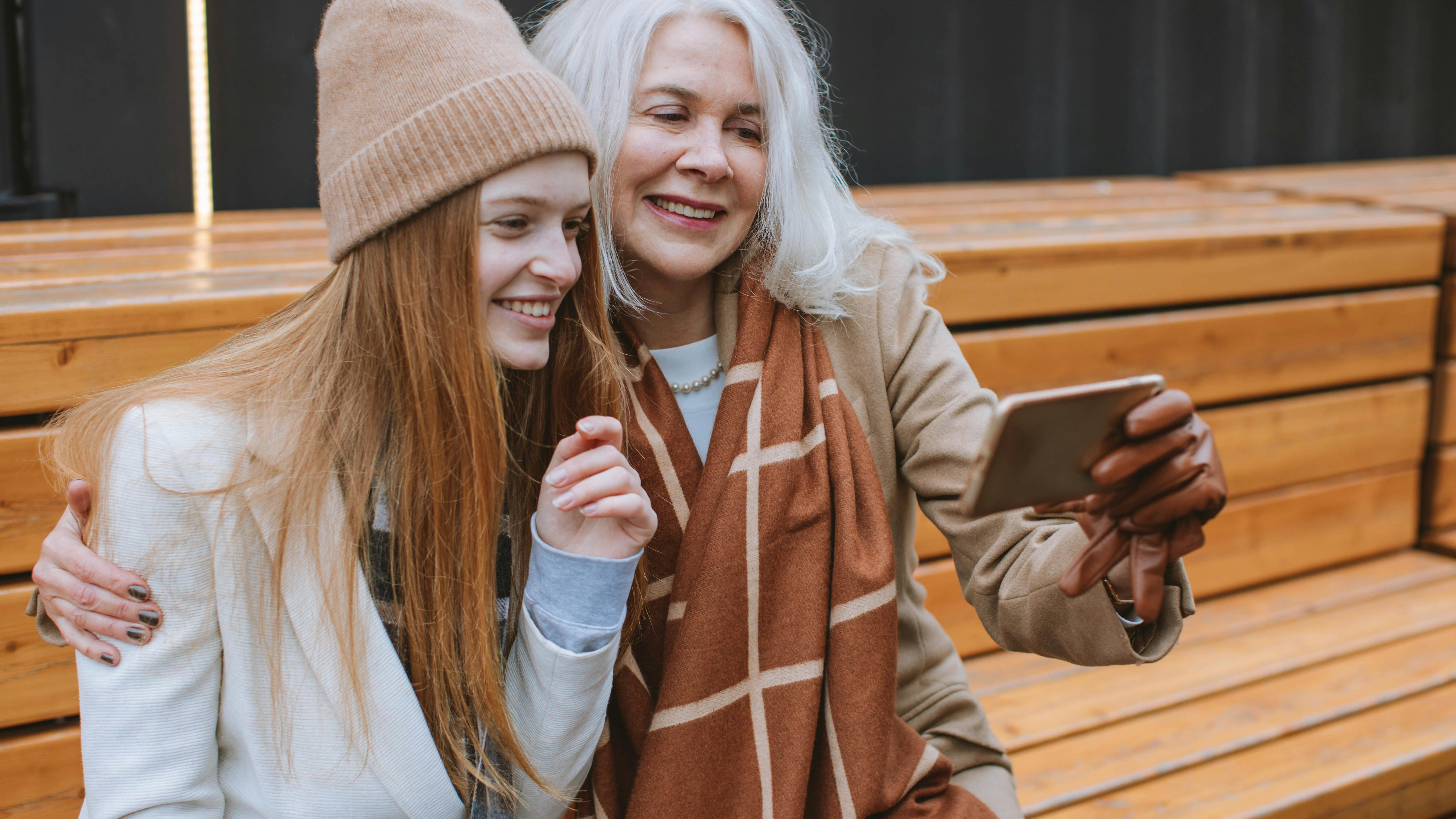 Middle aged woman with daughter sitting outside and sharing a moment on a mobile phone