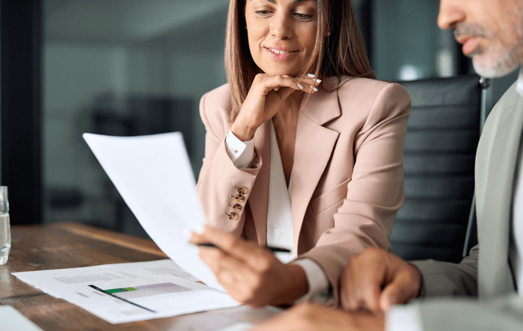 Woman in pink suit reviewing document at a desk with man in green suit