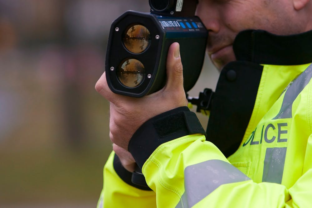 image of police officer using a radar gun to determine speed of vehicles traveling on roadway