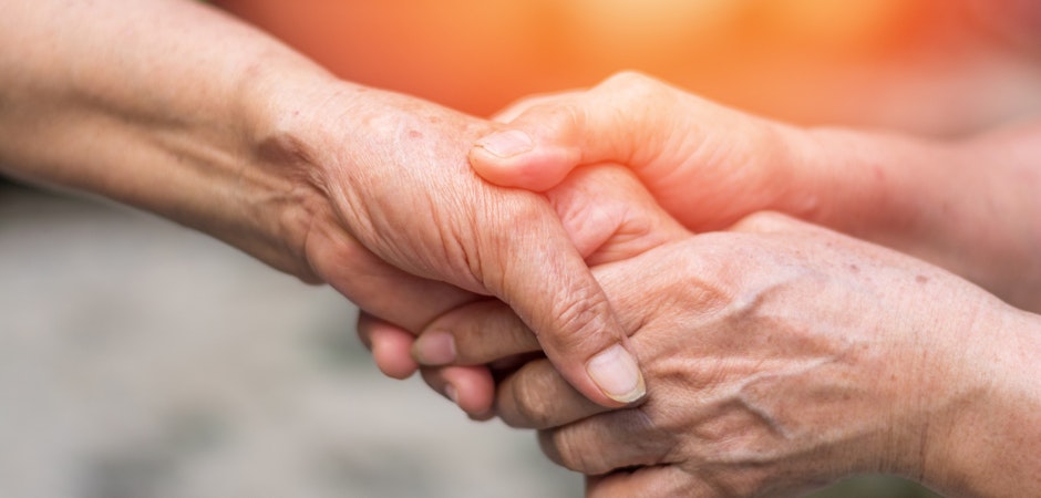 a young adult holding the hands of an elderly nursing home resident