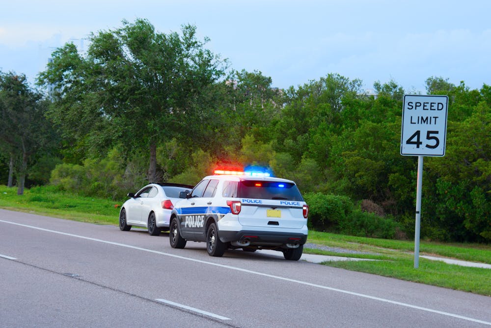 image of police vehicle with emergency lights on parked behind white car on the side of the road.